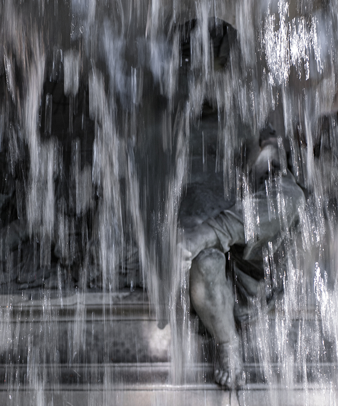Derrière un rideau formé par l’eau de la fontaine publique, l’enfant a l’air de jouer à cache-cache.